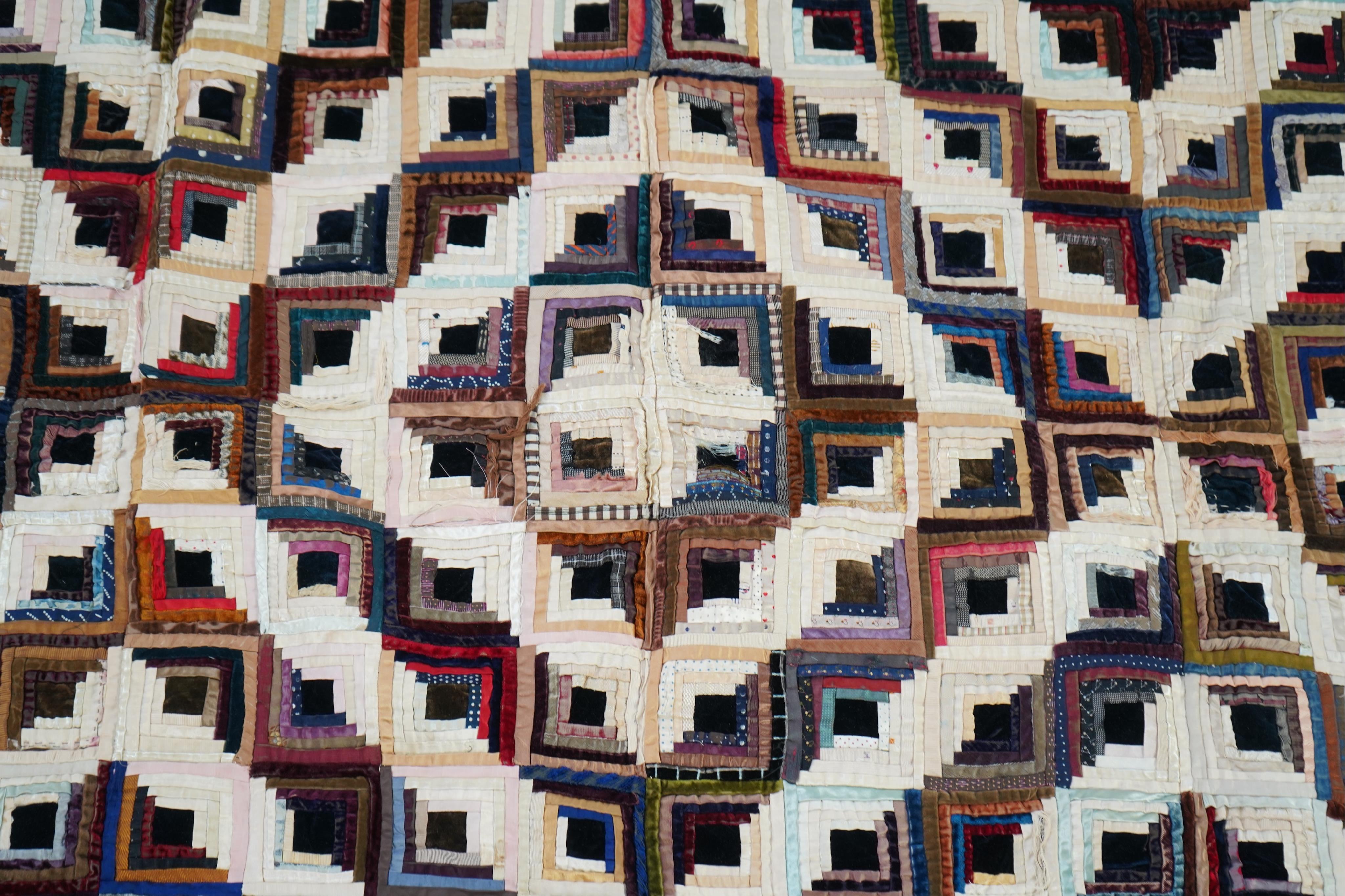 An early 20th century silk and velvet ‘Log Cabin’ designed bed cover, with a deep purple cotton backing, 140cm x 74cm. Condition - various thin strips have torn or are worn from constant use, so needs restoration.